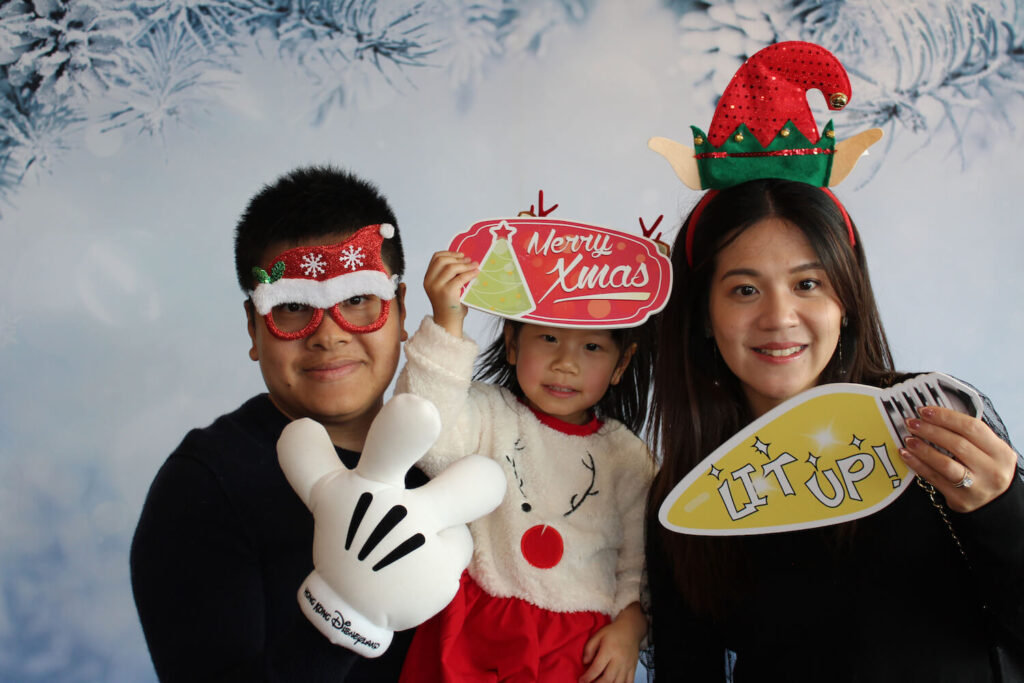 Mom and dad with their daughter using christmas props in front of a winter wonderland photobooth backdrop