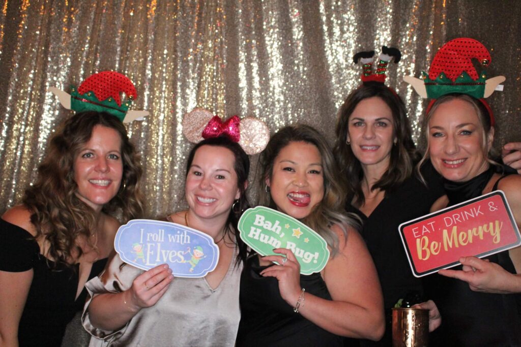 Friends posing with christmas photo booth props at corporate event
